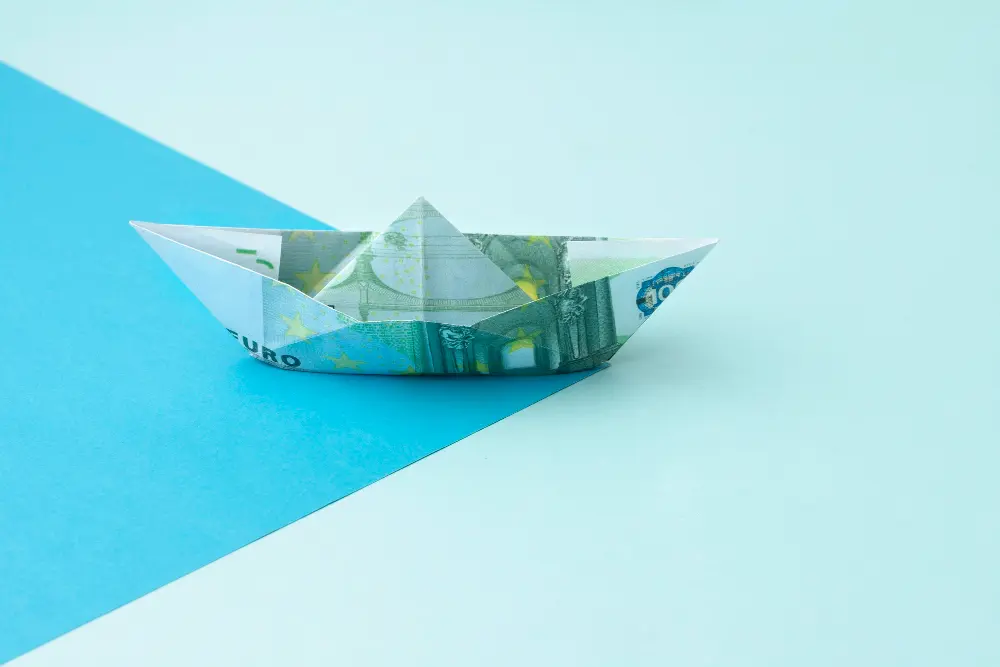 A banknote folded into a boat, representing capital for coastal resilience