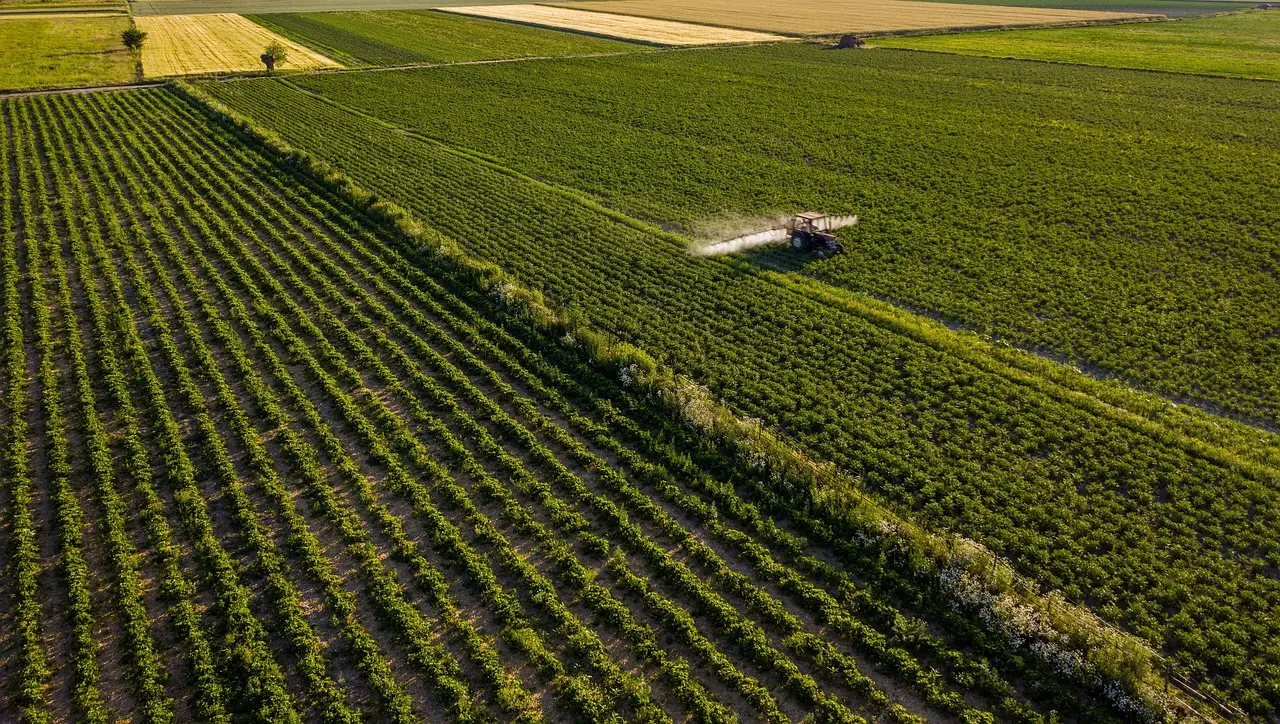 Aerial view of a tractor moving across parallel rows in an agricultural field
