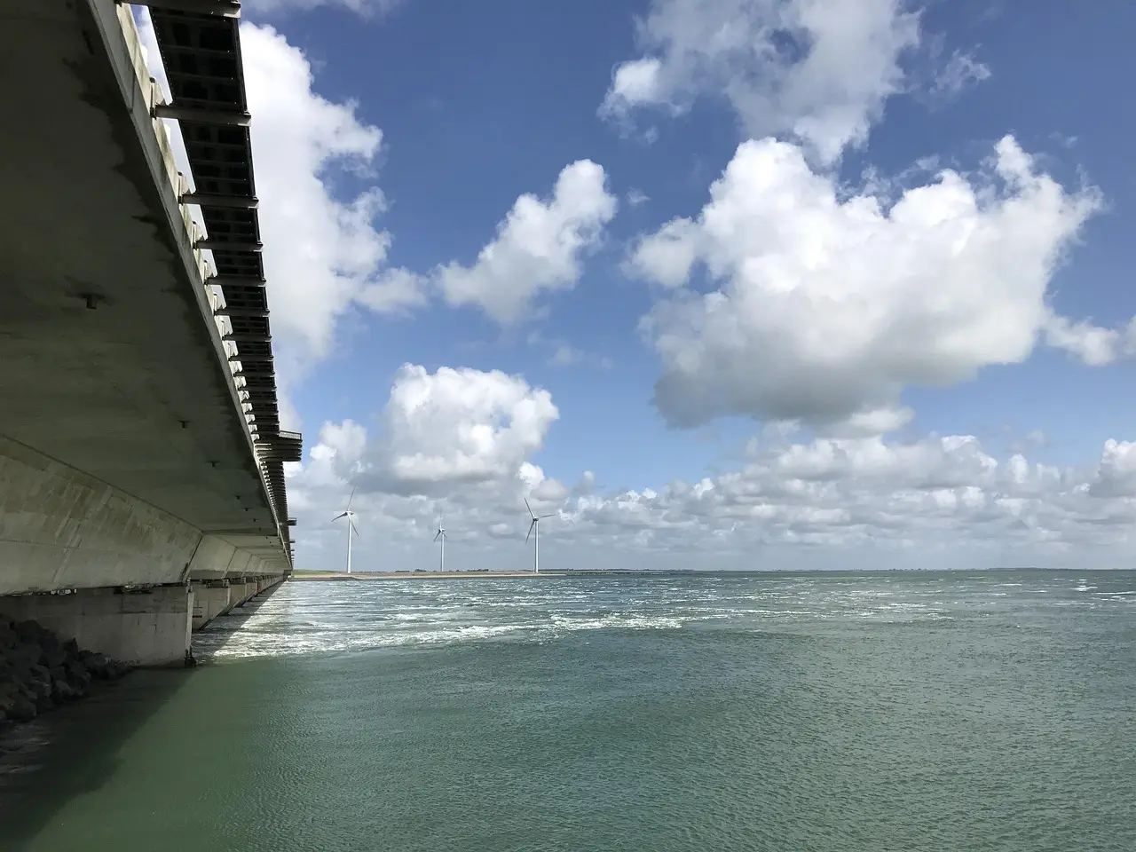 Concrete storm surge barrier at Neeltje Jans beside open water and distant wind turbines