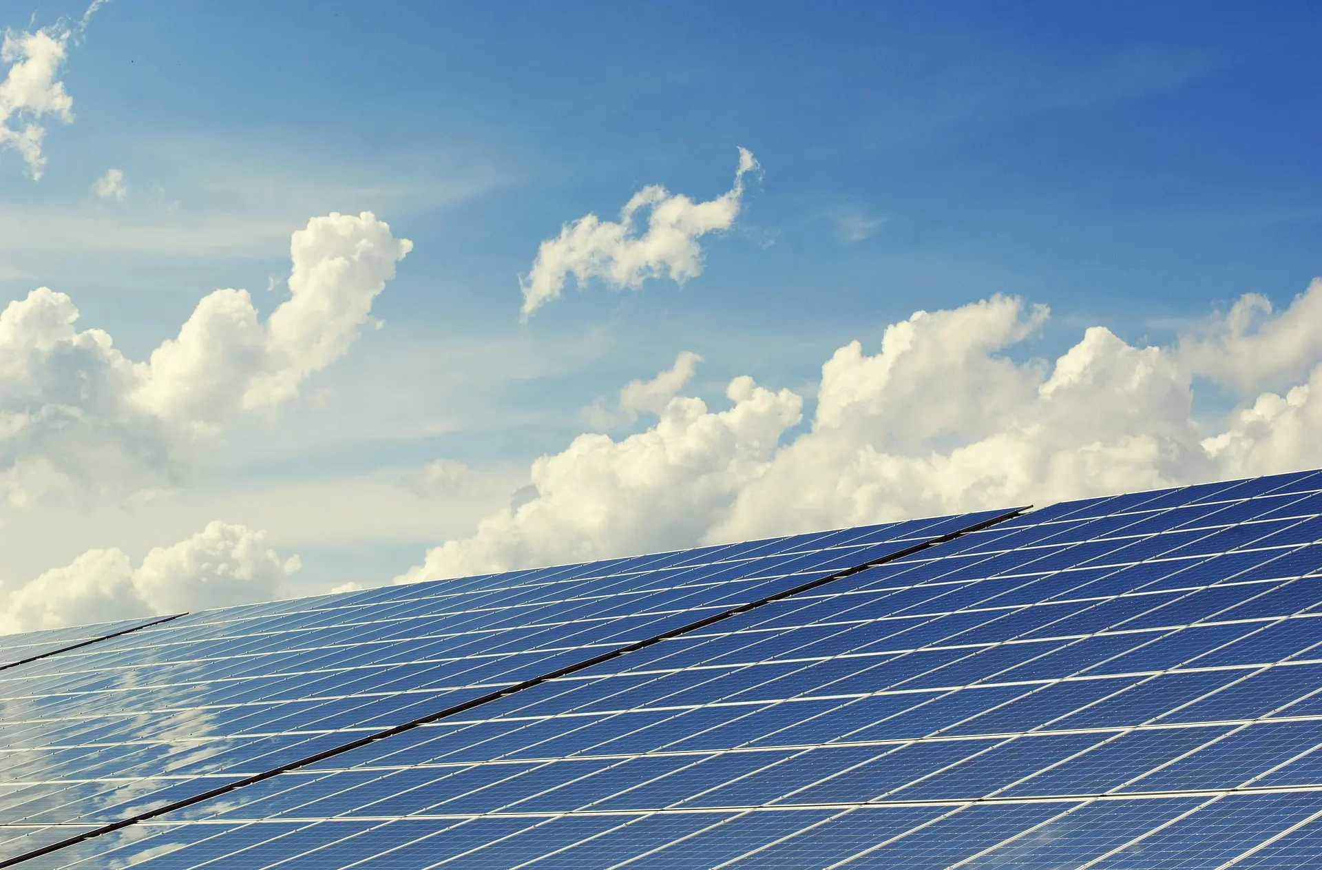 Rows of blue solar panels beneath a bright sky with white clouds