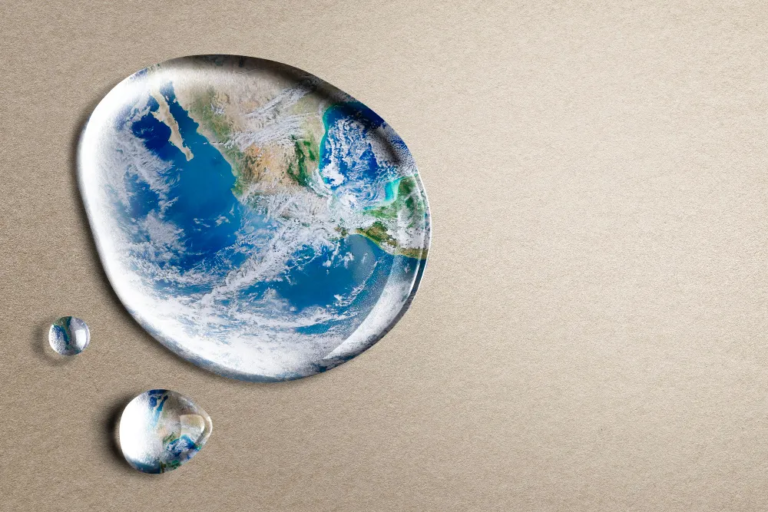 Water droplets shaped like Earth on a neutral surface, symbolizing global water security and climate resilience.